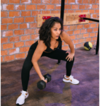 Midlife age woman wearing black workout leggings and black tank top in a somewhat squatted position holding black dumbbell doing a bicep curl while strength training.