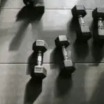 Closeup of two sets of black dumbbells used for strength training sitting on a black workout mat.