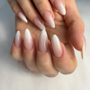 A close-up of a womans painted fingernails. Nails are medium to long length and are oval shaped. The nail color is a ombre blended french manicure with the milky jelly polish tips and a high gloss finish.